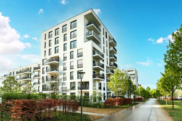 Modern apartment building with balconies, surrounded by landscaped gardens and a clear blue sky.