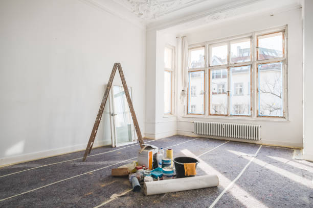 Bright, empty room undergoing renovations with tools and paint supplies scattered on the floor.