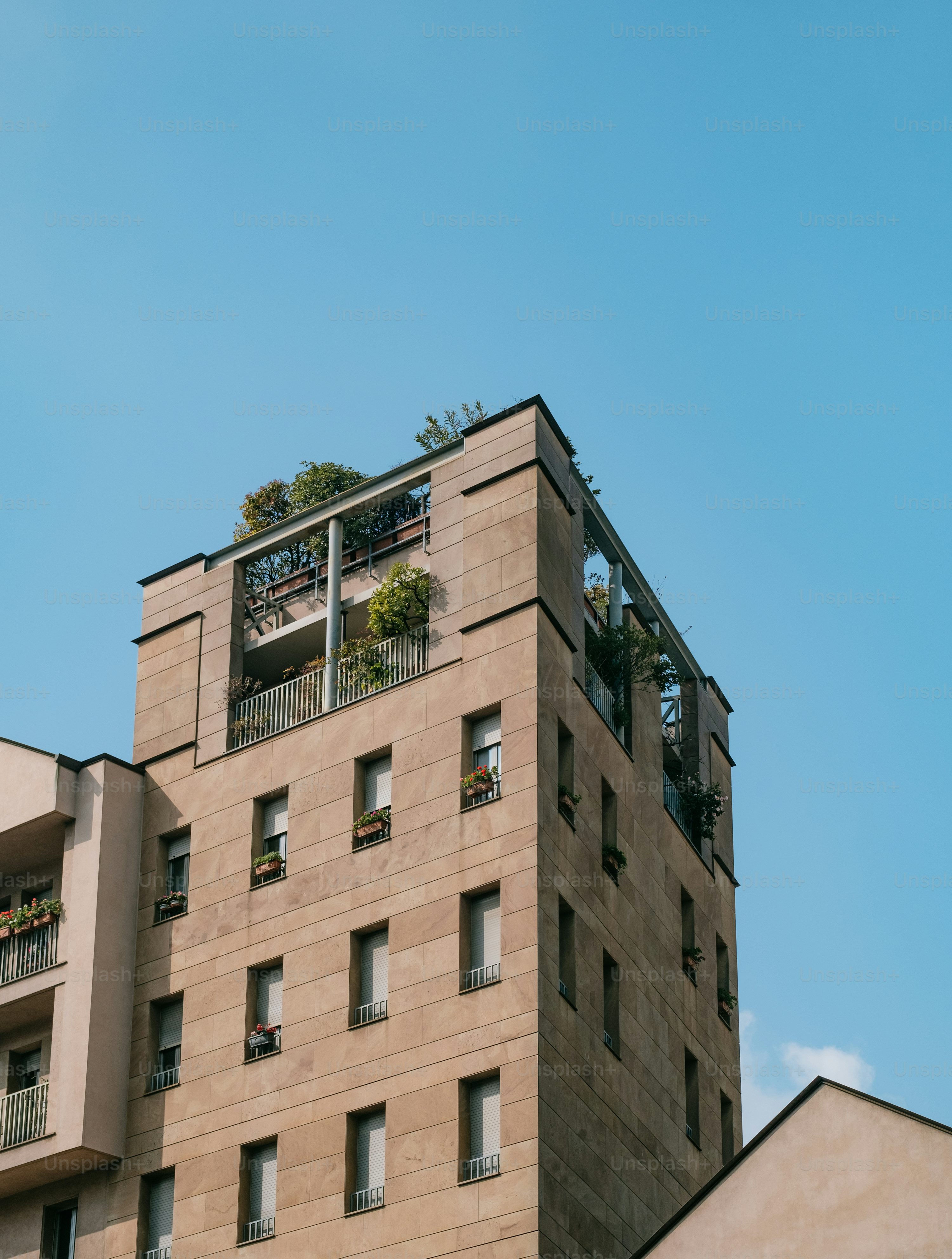 Modern apartment building with greenery on the rooftop under a clear blue sky.