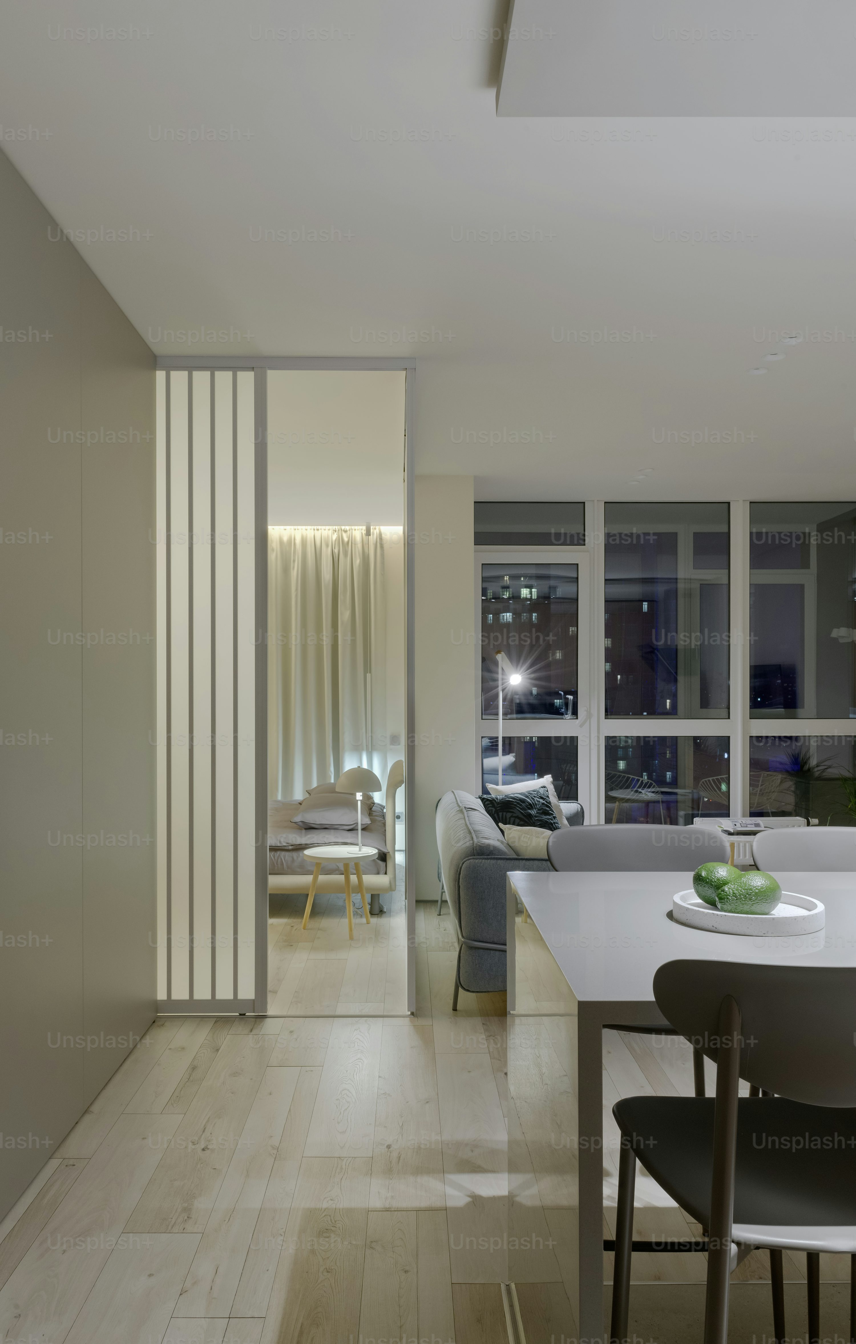 Modern living space featuring a dining area, cozy lounge, and a glimpse of a bedroom with soft lighting.