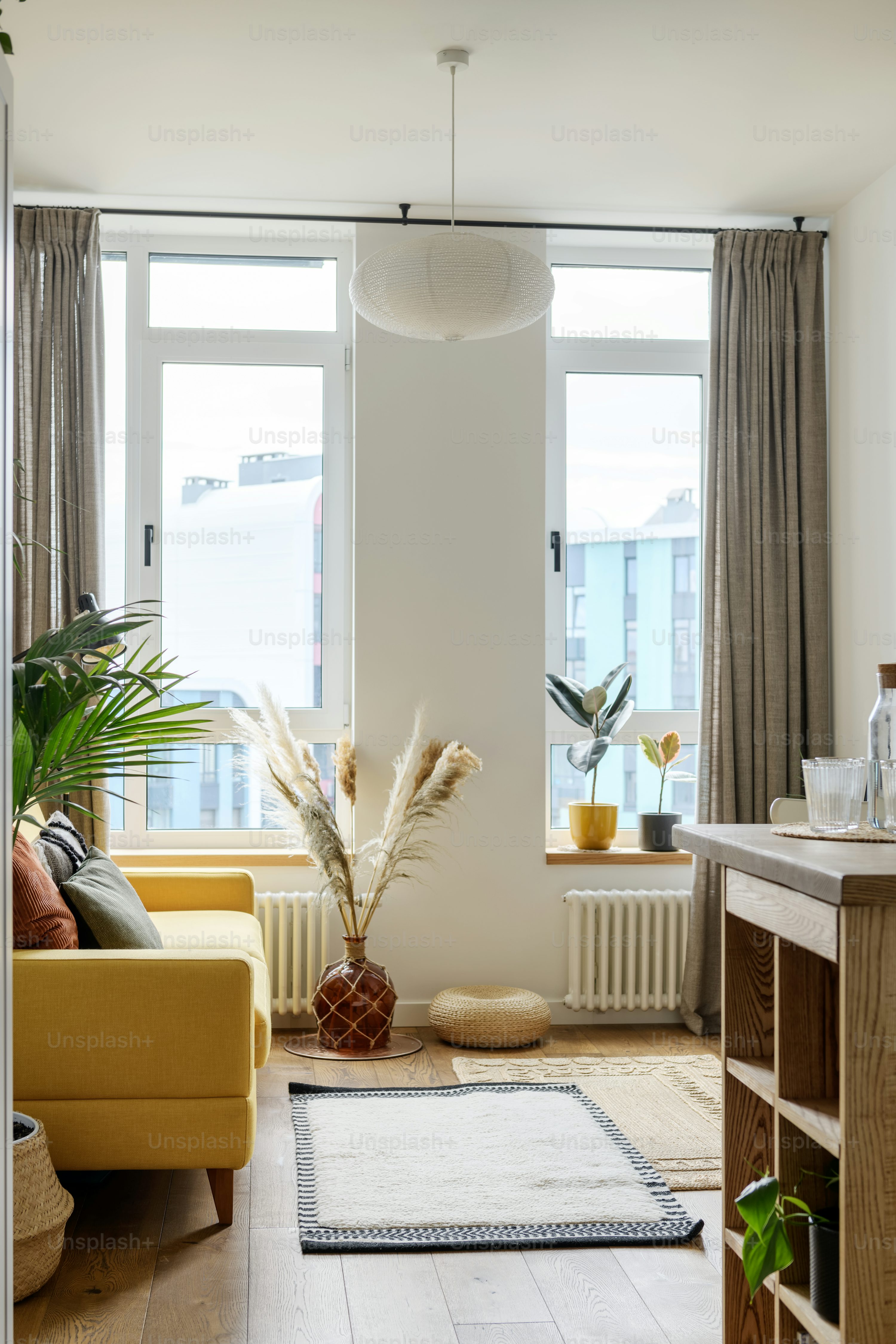 Bright and stylish living room with a yellow sofa, decorative plants, and large windows.
